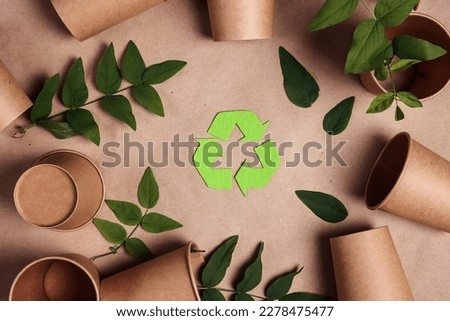 Green arrows recycle symbol with disposable empty paper coffee cups and green leaves on brown paper background. Environmentally friendly, disposable and zero waste concept. Royalty-Free Stock Photo #2278475477
