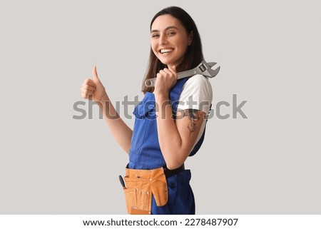 Female plumber with wrench showing thumb-up on grey background Royalty-Free Stock Photo #2278487907
