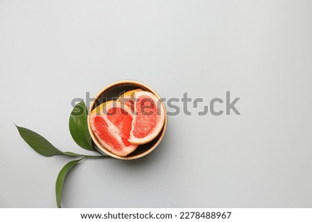 Bowl with pieces of ripe grapefruit and plant branch on light background