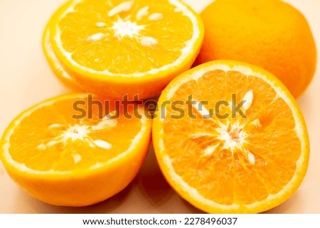 Oranges on a pink background. One orange is cut in half close up, the other is whole.