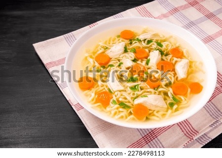 Homemade chicken soup with noodles and vegetables in a white bowl, on a  black  background. Healthy warm comfortable food.