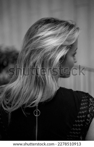 Portrait Of Beautiful Young Blond Woman With Long Wavy Hair. Back View Female back with long, curly, natural blonde hair, in black dress, on grey background