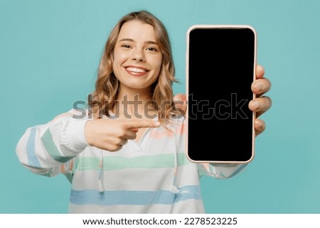 Young fun blonde woman wear striped hoody hold in hand use point index finger on close up mobile cell phone with blank screen workspace area isolated on plain pastel light blue cyan background studio