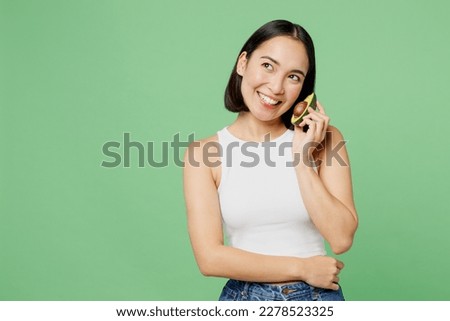 Young happy woman wear white clothes hold half of avocado pov speak on mobile cell phone isolated on plain pastel light green background. Proper nutrition healthy fast food unhealthy choice concept