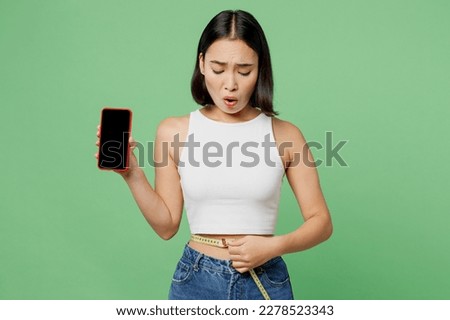Young sad woman wear white clothes use blank screen mobile cell phone hold measure tape on waist isolated on plain pastel light green background Proper nutrition healthy fast food choice concept