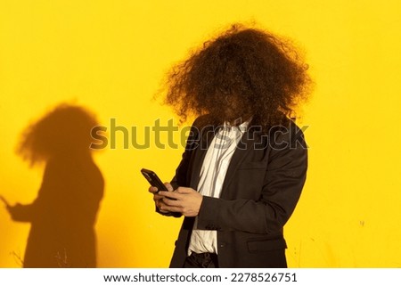 portrait of unrecognizable long-haired businessman with cellphone over yellow background