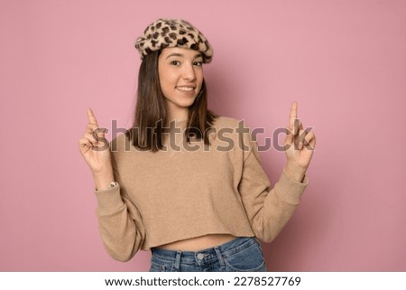 Successful friendly looking Young european brunette woman on pink background exclaiming excitedly, pointing both index fingers up, indicating something.