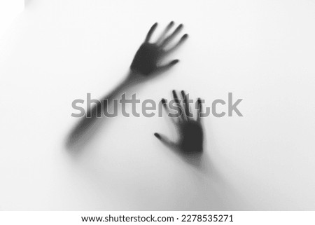 Defocused hand silhouette behind frosted glass in black and white mode, halloween concept