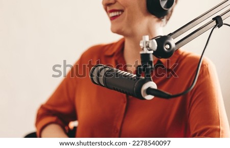 Happy woman smiling and looking away while sitting behind a microphone with headsets. Cheerful woman interviewing a guest while hosting a live radio show in a broadcast studio.