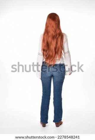 full length portrait of beautiful woman model with long red hair, wearing casual outfit white blouse  top and denim jeans, isolated on white studio background. Backwards standing pose, walking away fr