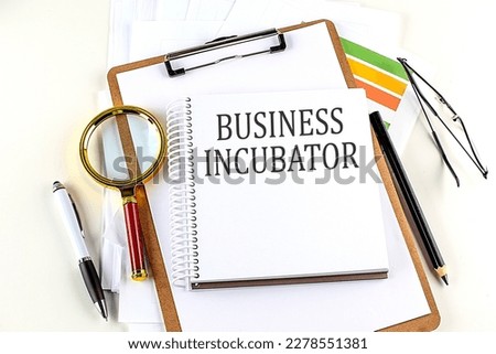 BUSINESS INCUBATOR text on a notebook with clipboard on white background