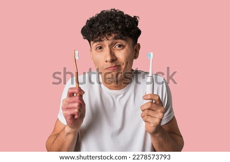A young man compares manual vs electric toothbrush for optimal dental care - weighing effectiveness, convenience, and cost. Royalty-Free Stock Photo #2278573793