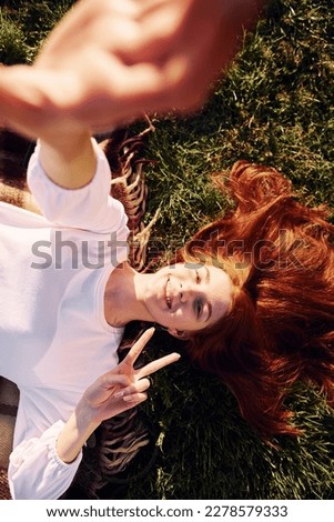 Laying down and making a selfie. Top view. Young girl is on the field at sunny daytime having nice weekend.