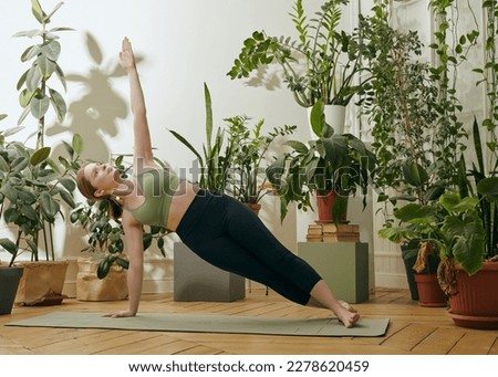 a woman does yoga at home on a rug surrounded by green plants performing an asana