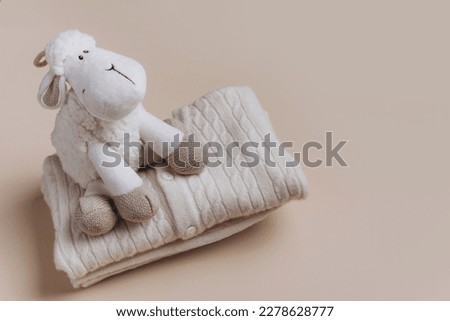 Sheep toy on stack of merino wool baby clothes over beige background. Newborn gifts for Christmas and baby shower, care package, donation, charity, donation idea. Banner. Top view. Copy space.