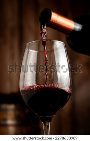 red wine glass with bottle serving wine on still life table with wooden barrel grapes and cheese on wooden boards