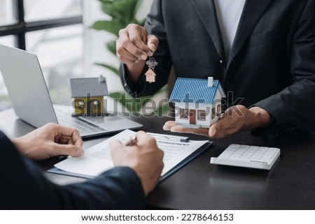Real estate agents, insurance sales agents, and young Asian businessmen handing home keys and model homes to homebuyers after signing sales contracts are satisfied in the office.