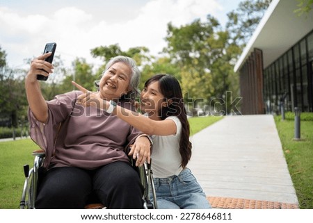 Happy Asian patients in a wheelchair use smartphones to take pictures with careful caregivers or nurse Concept of happy retirement with care from a caregiver and Savings and senior health insurance.