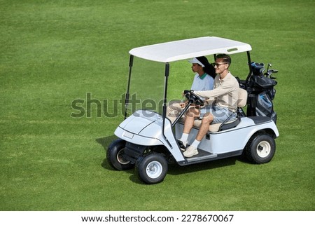 High angle view at sporty couple driving golf cart on green field minimal, copy space Royalty-Free Stock Photo #2278670067