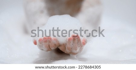 Close-up bubble foam on boy hands surrounded by soap suds when taking a bath in bathtub. Funny, healthcare lifestyle and hygiene concept