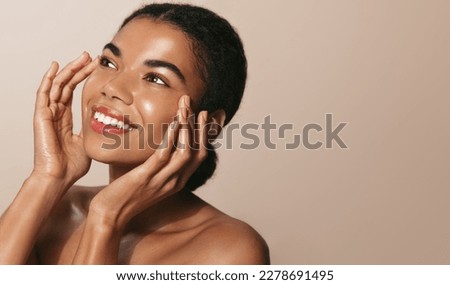 Young african american girl with clear, glowing facial skin, washes her face with cosmetic product, smiling and looking up, enjoys smooth feeling after hydrating serum, face mask Royalty-Free Stock Photo #2278691495