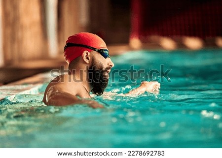A young man swims crawl in the pool in a hat and goggles for swimming, training in the pool Royalty-Free Stock Photo #2278692783