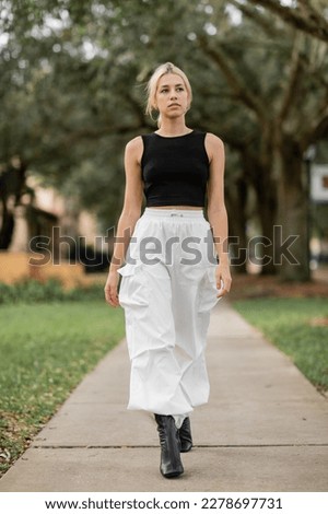full length of young woman in white cargo pants and black tank top walking on green street in Miami Royalty-Free Stock Photo #2278697731