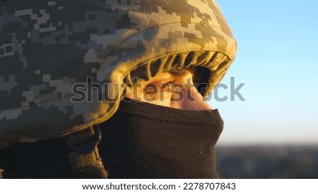 Gaze of male ukrainian army soldier in helmet and balaclava outdoor. Profile view of young military man looking with hope at sunset. Invasion resistance. War between Russia and Ukraine. Close up.