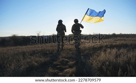 Young soldiers of ukrainian army running with lifted national banner on field. Military woman and man in camouflage uniform jogs with waving flag of Ukraine on meadow. Resistance to russian invasion.