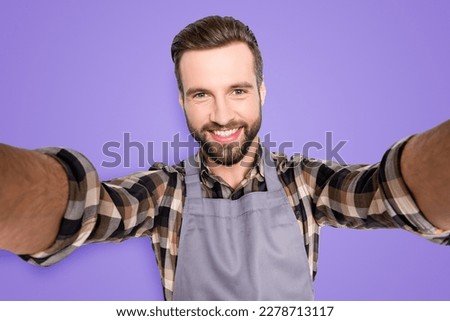 Self portrait of trendy stylish baker with hairstyle shooting selfie on smart phone with two hands, isolated on grey background, having video-call during break pause timeout