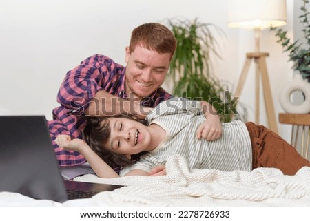 delightful moment between father and son, filled with laughter and love as they play together on the bed. Joyful dad and child bonding through playful tickles, creating a warm, happy atmosphere.