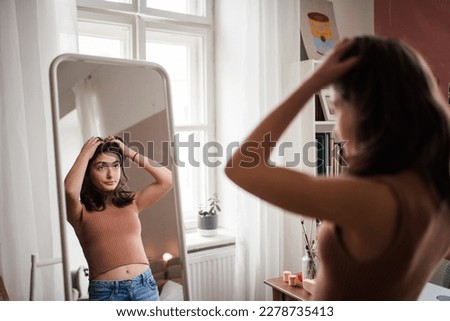 Young teenage girl looking in the mirror in her room. Royalty-Free Stock Photo #2278735413