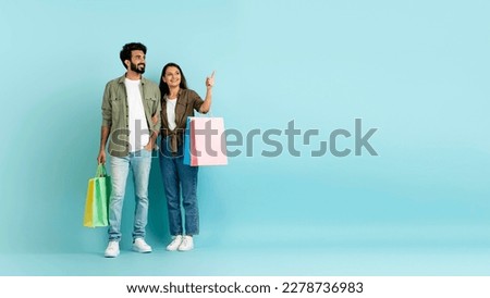 Sale, black friday, discount. Loving happy millennial multicultural couple in casual go shopping together, pretty eastern woman showing her handsome arab husband copy space, blue background, banner