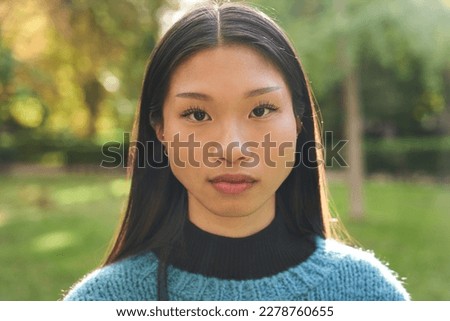 Portrait of beautiful young Asian girl with serious countenance looking at camera outdoors. Front view of earnest Chinese girl. Confident people posing in the park for photo.  Royalty-Free Stock Photo #2278760655
