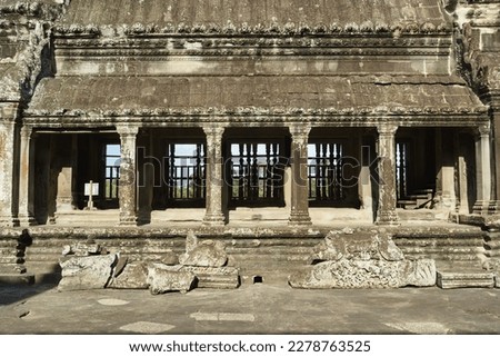 A photo of the sandstone buildings at one side of a courtyard at the top of the temple mountain at Angkor Wat. Intricate carvings and bas reliefs can be seen all over the heavily weathered stone. 