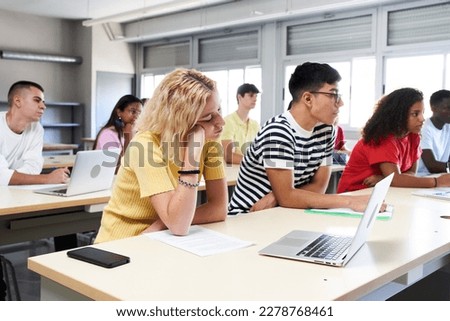 Bored student attending in class with a laptop at high school classroom. Group of students of a university. . High quality photo