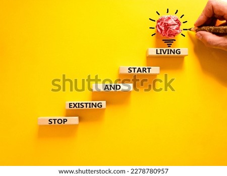 Stop existing start living symbol. Concept words Stop existing and start living on wooden blocks. Beautiful yellow table yellow background. Business Stop existing start living concept. Copy space.