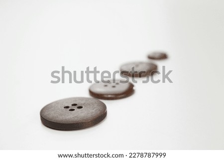 A shallow focus row of isolated brown wooden buttons with different textures lying flat in one line on a bright white table background surface. 