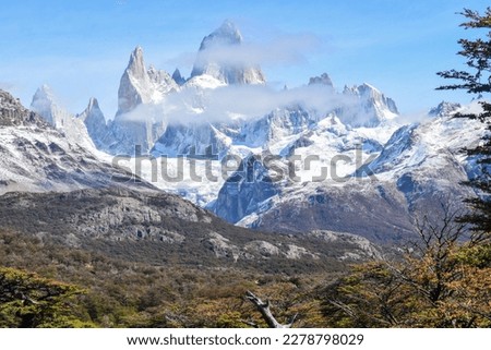 this picture was capture with the clouds hanging low at the beautiful Fitz Roy mountain with snow covering the landscape and colorful trees at the bottom of the hiking pathway. 