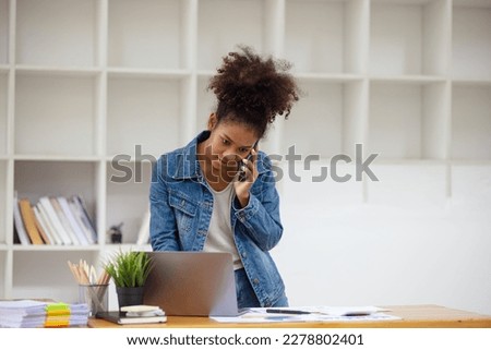 Young African American businesswoman working on smart phone and laptop computer with pile of documents workplace, business finance and accounting concepts.