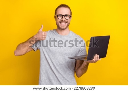 Photo of cheerful satisfied man wear stylish clothes hold netbook thumb up nice choice sale device shop isolated on yellow color background