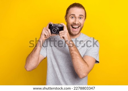 Photo of excited funky man wear grey t-shirt holding camera tacking photo isolated yellow color background