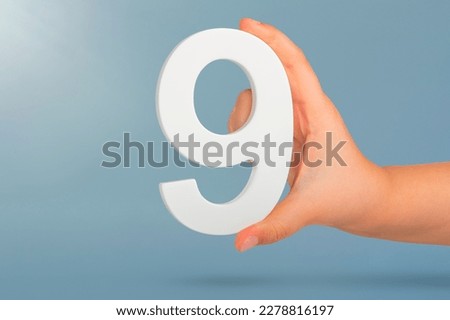Number nine in hand. A hand holds a white number 9 on a blue background. Concept with number nine. Birthday 9 years, percentage, ninth grade or day. Royalty-Free Stock Photo #2278816197