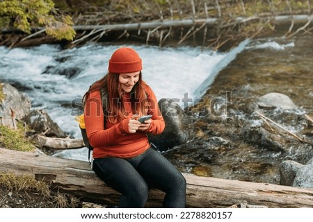 Stylish woman holding phone with green backpack and relaxing on nature background. Travel and wanderlust concept. Amazing chill moment in the forest