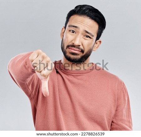 Sad, disappointment and portrait of an Asian man with a thumbs down isolated on a studio background. Review, unhappy and a Chinese guy with a hand sign for a problem, mistake and dislike emoji Royalty-Free Stock Photo #2278826539