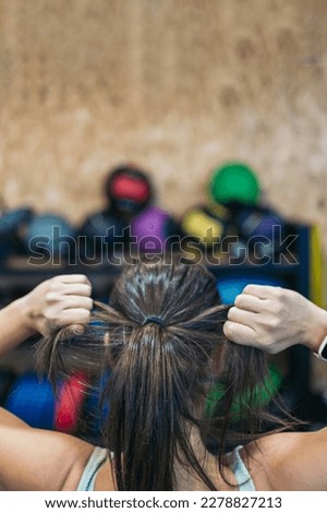 Vertical image of a young athletic woman on her back in the gym adjusting her hair in a ponytail.