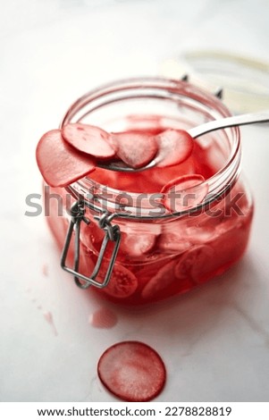 Jar of pickled thinly sliced pink radishes. A spoon is sticking out of the jar. White background. Korean dish. Royalty-Free Stock Photo #2278828819