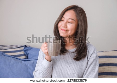 Portrait image of a young woman with closed eyes holding and drinking hot coffee at home