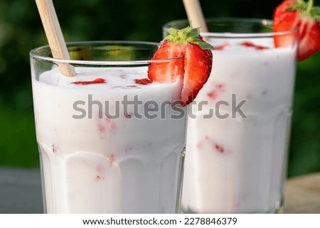 Strawberry smoothie in two glass glasses and fresh strawberries on a wooden table in the yard, close up