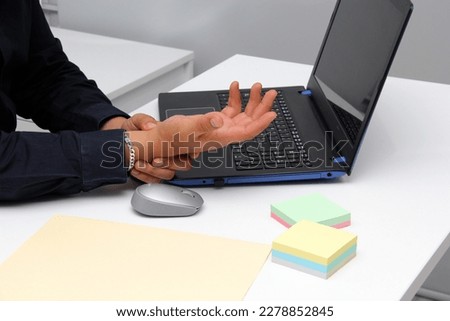 Adult Latin man suffering from pain, tingling, numbness and weakness in his wrist due to Carpal Tunnel Syndrome while working in his office with his laptop and mouse